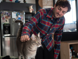 Homme souriant caressant son chat gris &agrave; la maison