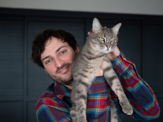 Chat gris tigr&eacute; grognon port&eacute; par son ma&icirc;tre heureux