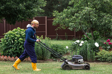 A lawn mower man mows the grass in the backyard. Agricultural machinery for garden maintenance. The...
