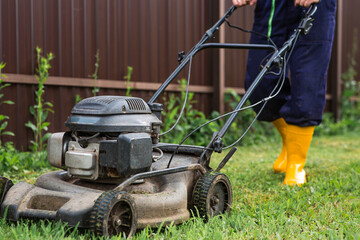 Fototapeta premium A lawn mower man mows the grass in the backyard. Agricultural machinery for garden maintenance. The concept of gardening and country life. The banner.