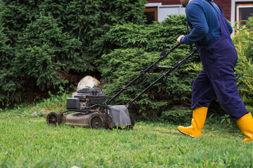 A lawn mower man mows the grass in the backyard. Agricultural machinery for garden maintenance. The...