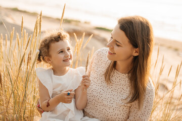A loving mother and her happy daughter share a tender moment in sun-kissed tall grasses, both smiling.