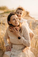 A loving mother and her happy daughter share a tender moment in sun-kissed tall grasses, both...