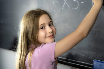 Young student writing a multiplication on the blackboard