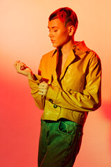 young woman with short styled hair wearing yellow jacket and green pants posing thoughtfully...
