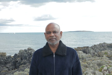 Portrait of a middle-aged man in a navy fleece jacket standing by the rugged Irish coastline under...