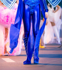 Close-up shot of girls' legs in colorful carnival costumes at the Nha Trang Sea Festival carnival. Shiny fabrics, feathers, heels, movement, evening light, festive atmosphere