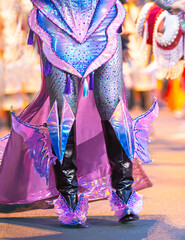 Close-up shot of girls' legs in colorful carnival costumes at the Nha Trang Sea Festival carnival. Shiny fabrics, feathers, heels, movement, evening light, festive atmosphere