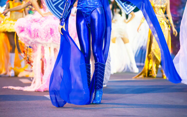 Close-up shot of girls' legs in colorful carnival costumes at the Nha Trang Sea Festival carnival. Shiny fabrics, feathers, heels, movement, evening light, festive atmosphere