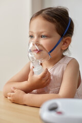 cute little toddler girl inhaling medicine on nebulizer and holding it on her own