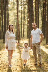 Fototapeta premium Family couple and daughter stands together in sunny lighted forest during sunset 