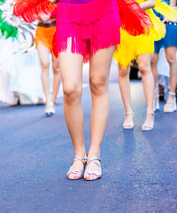 Close-up shot of girls' legs in colorful carnival costumes at the Nha Trang Sea Festival carnival. Shiny fabrics, feathers, heels, movement, evening light, festive atmosphere