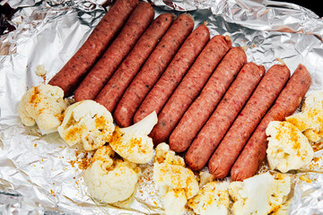 Grilling sausages with seasoned cauliflower at an outdoor barbecue in summer