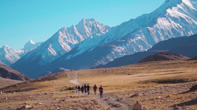 Rear view shot of group of people walking towards the snowy Himalayan mountain peak near Chandratal Lake in Spiti Valley, Himachal Pradesh, India. Group of hikers walking in front of the Himalayas.	