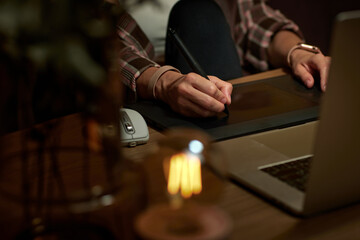 female hands with graphic tablet retouching photo on laptop computer at night