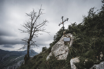 Scenic low-key mountain memorial site with an iron cross mounted on a rock and a blank stone...