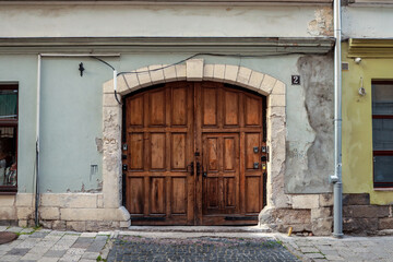 Old wooden arched door with stone frame on historic building facade, weathered wall textures and...
