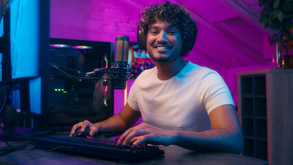Indian Latino Muslim Arabian man talking microphone looking at camera smile influencer streamer male guy gamer playing computer cyber sport online streaming games blogger headphones neon light addict
