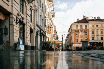 Historic European street with pastel buildings, wet reflective pavement, yellow umbrella at a...