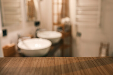 Wooden countertop in the foreground with a blurred view of a modern bathroom featuring two white...