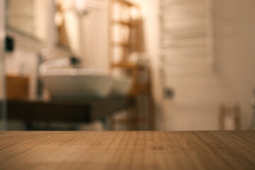 Wooden countertop in the foreground with a blurred view of a modern bathroom featuring two white...