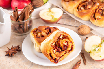 Apple cinnamon roll, sweet cinnabon buns with apple filling. Viral apple pie rolled buns, on beige table with cinnamon sticks, apples, nuts and spices