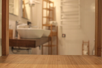 Wooden countertop in the foreground with a blurred view of a modern bathroom featuring two white...