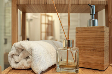 Close-up of a wooden bathroom shelf with a rolled towel, bamboo soap dispenser, and reed diffuser....