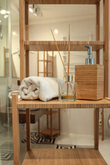Close-up of a wooden bathroom shelf with a rolled towel, bamboo soap dispenser, and reed diffuser....