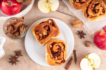 Fototapeta premium Apple cinnamon roll, sweet cinnabon buns with apple filling. Viral apple pie rolled buns, on beige table with cinnamon sticks, apples, nuts and spices
