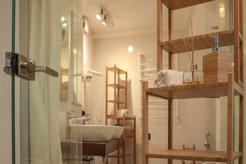 Bright modern bathroom interior with wooden shelving, rolled towel, fragrance diffuser, and soap...