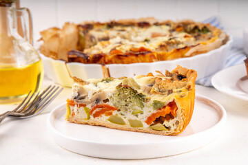 Slice of freshly baked homemade pie quiche lorraine on white table, top view, copy space. Vegan quich tart pie with mushrooms, tomatoes, zucchini, spinach and cheese