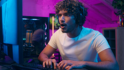 Concentrated happy Arabian Indian Muslim man typing code keyboard computer games playing video game...