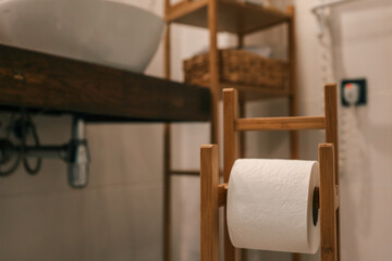 Stylish modern bathroom with wooden toilet paper holder, white ceramic toilet, towel rack, sink,...