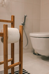 Close-up of a wooden toilet paper holder with white toilet paper roll, modern bathroom in soft...