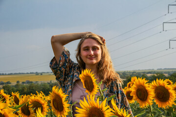 young blond woman among sunflowers in the field, doing her hair, straightening her hair with her...