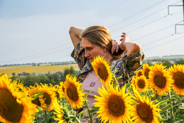 young blond woman among sunflowers in the field, doing her hair, straightening her hair with her hands, waist-length portrait, large yellow flowers
