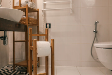 Stylish modern bathroom with wooden toilet paper holder, white ceramic toilet, towel rack, sink,...