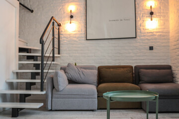 Loft-style living room with a green round coffee table in focus, a modular sofa in neutral colors,...