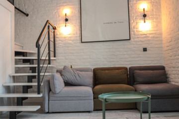 Loft-style living room with a green round coffee table in focus, a modular sofa in neutral colors,...