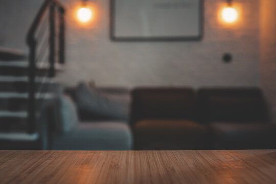 Modern loft interior with a close-up view of a wooden tabletop in focus. In the blurred background: a cozy modular sofa, spiral staircase, white brick wall, and warm wall sconces