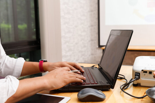 Close-up of a person typing on a laptop connected to a projector, preparing for a business presentation in a modern workspace.