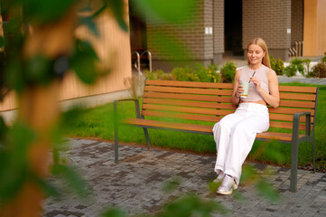 woman enjoying iced coffee on outdoor bench surrounded by greenery. casual, tranquil scene...