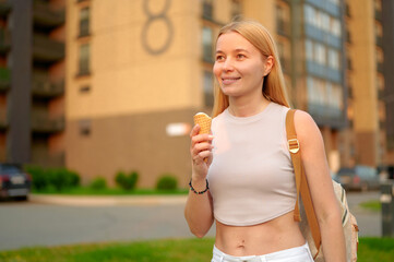 woman enjoying ice cream outdoors, smiling in urban setting. casual attire, backpack. warm weather, relaxed mood. modern city block background enhances leisure vibe