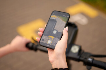 woman holding smartphone captures electric scooter handlebar while outdoors. urban mobility and tech focus highlight modern transportation trends and active lifestyle engagement.