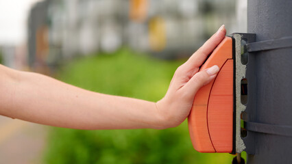 pressing pedestrian crossing button outdoors, close-up of hand interacting with orange signal...
