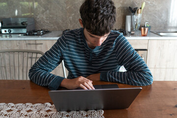 Teenager boy typing on a laptop computer at the kitchen table, high angle view