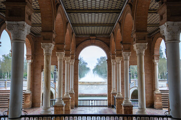 A majestic view through the arched gallery of Plaza de Espana in Seville Spain, showcasing the central fountain and surrounding architectural beauty.