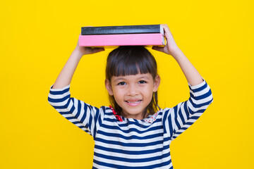 Cute asian girl holding books on head on yellow background