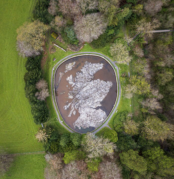 Aerial view of a reservoir shaped like Scotland reflects the sky amid lush trees, creating a striking contrast of natural and man-made elements, Peebles, Scotland, United Kingdom.